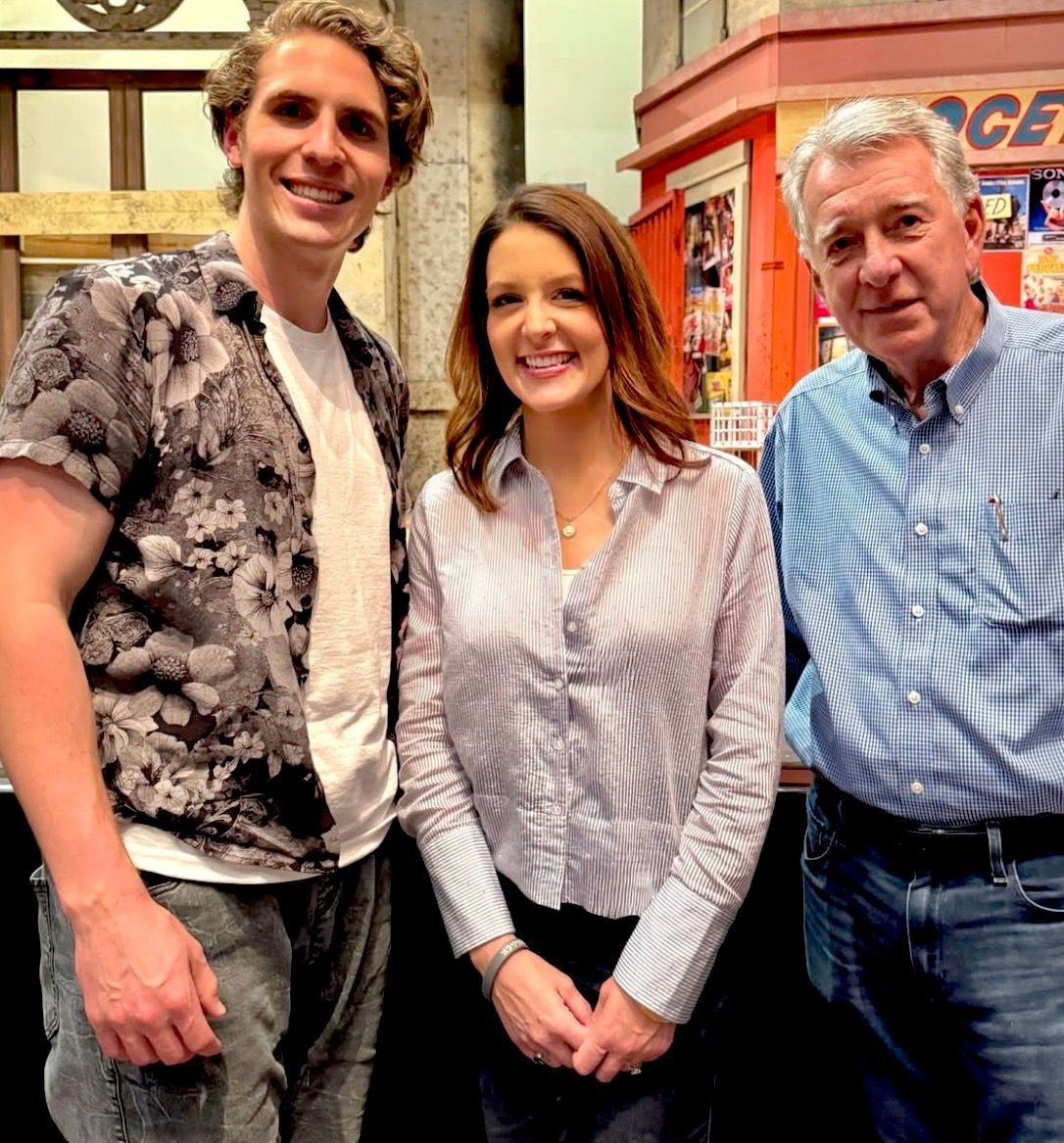 Three people standing together indoors, smiling in front of a colorful shop display.