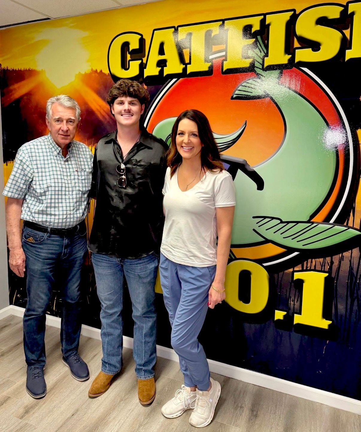 Three people posing in front of a CAT 101.1 radio station sign