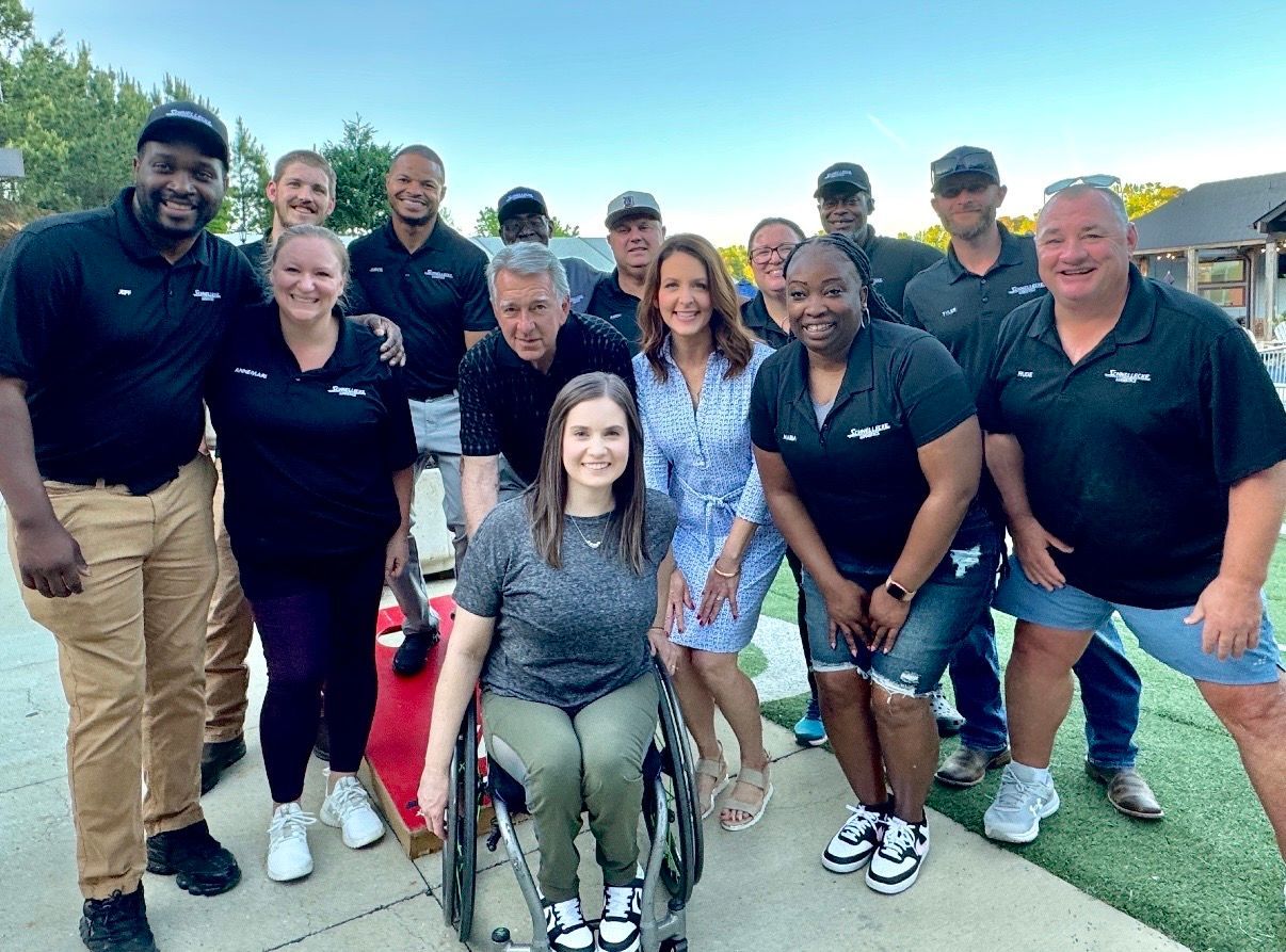 Group of people posing outdoors on a sports field, smiling in casual black and blue clothing.