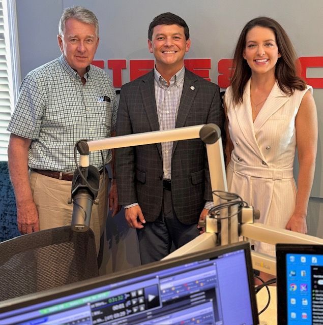 Three people posing in a radio studio behind microphones and monitors