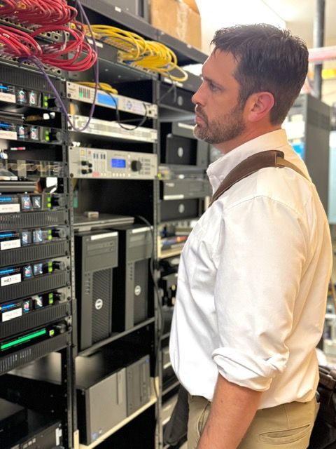 Technician standing beside a rack of network and server equipment, looking at the controls.