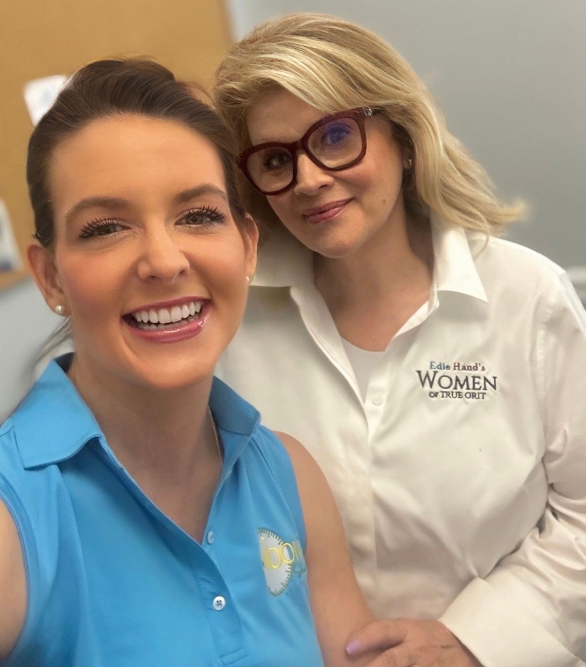 Two smiling coworkers posing indoors, one in a blue polo and one in a white Women’s shirt.