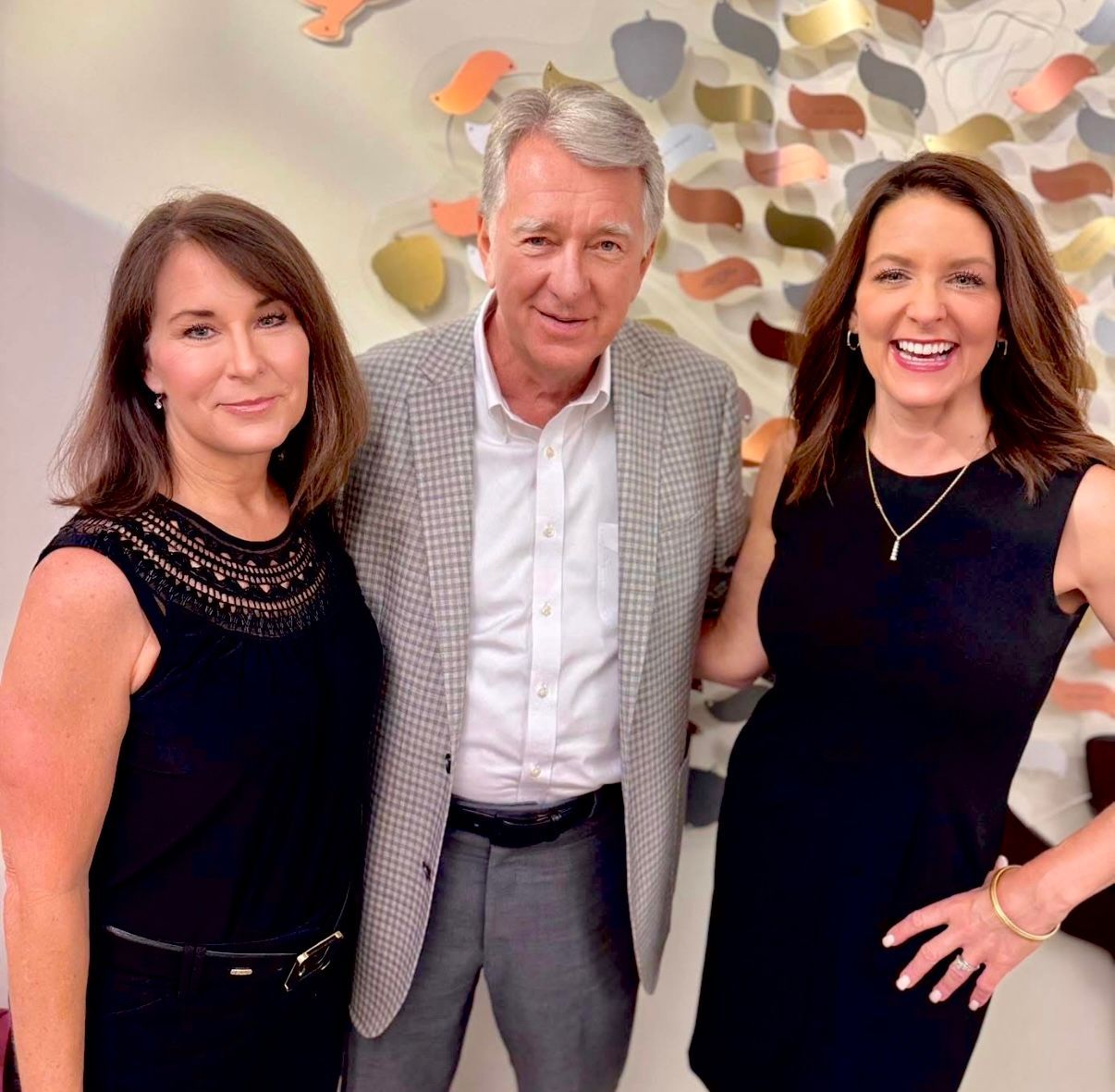 Three people smiling at an indoor event, with a patterned wall backdrop.