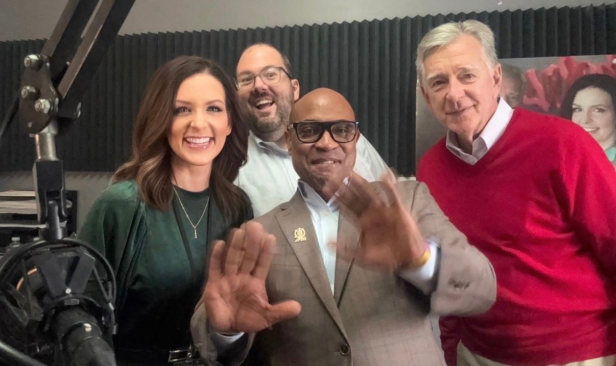 Four people smiling and posing in a studio, with one person in a red sweater on the right