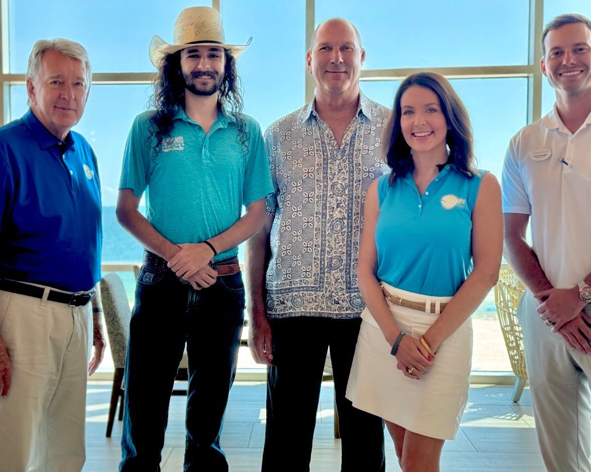 Five people posing indoors, smiling in front of large windows, wearing blue and patterned shirts.