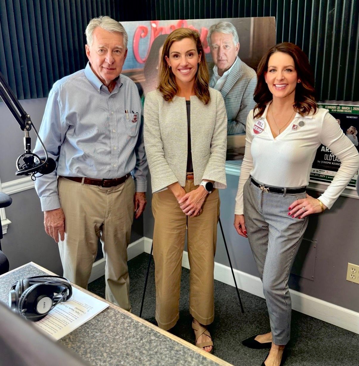 Four people posing in a radio studio with microphones and headphones on the desk.