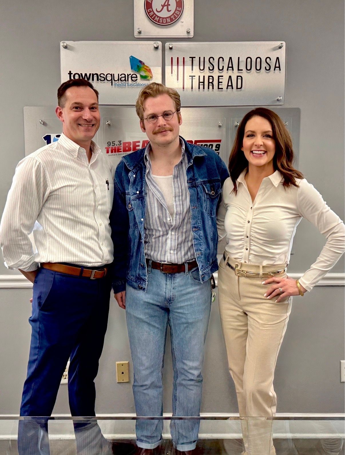 Three people posing indoors in front of office signs, smiling at the camera.