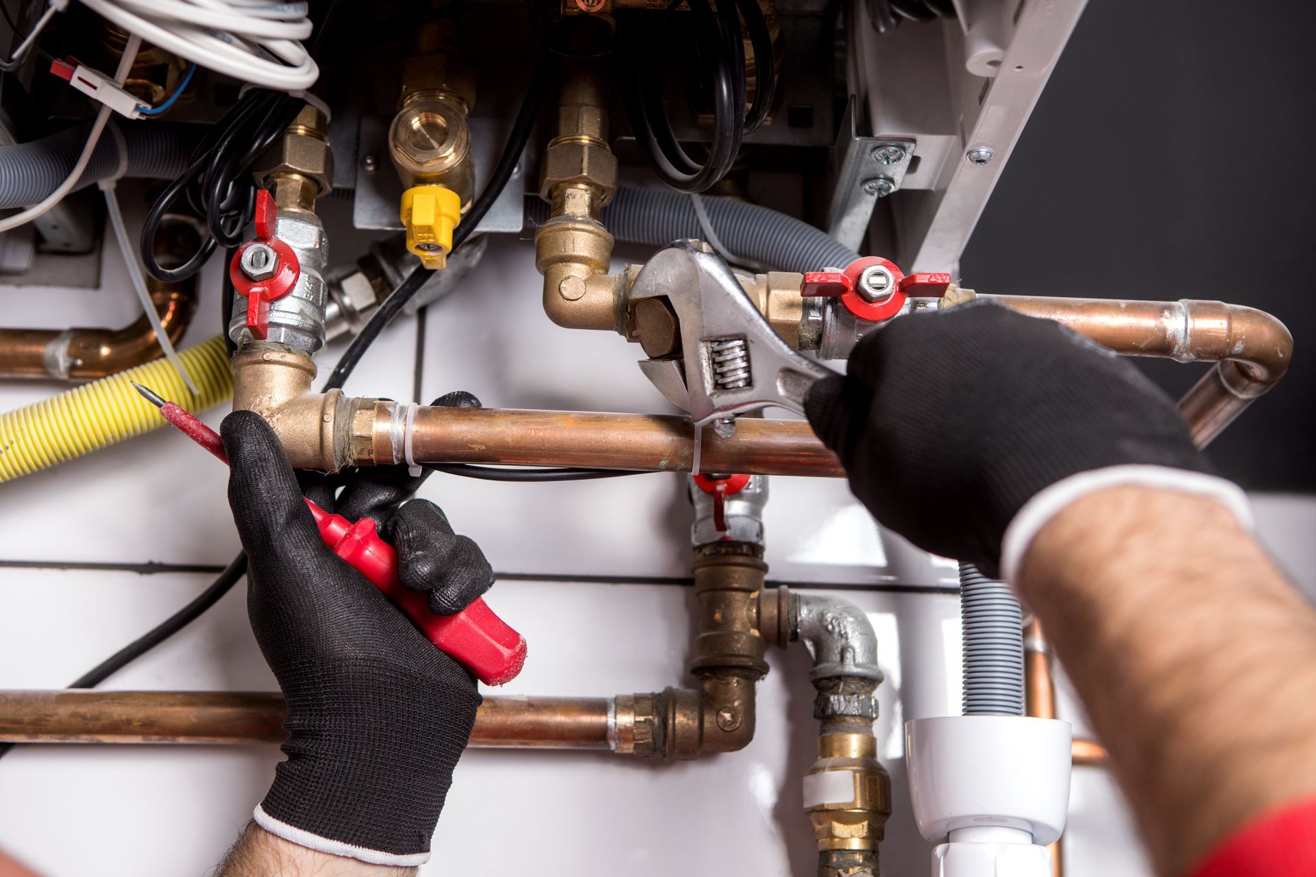 Worker black gloves working on copper pipes with a wrench and screwdriver.