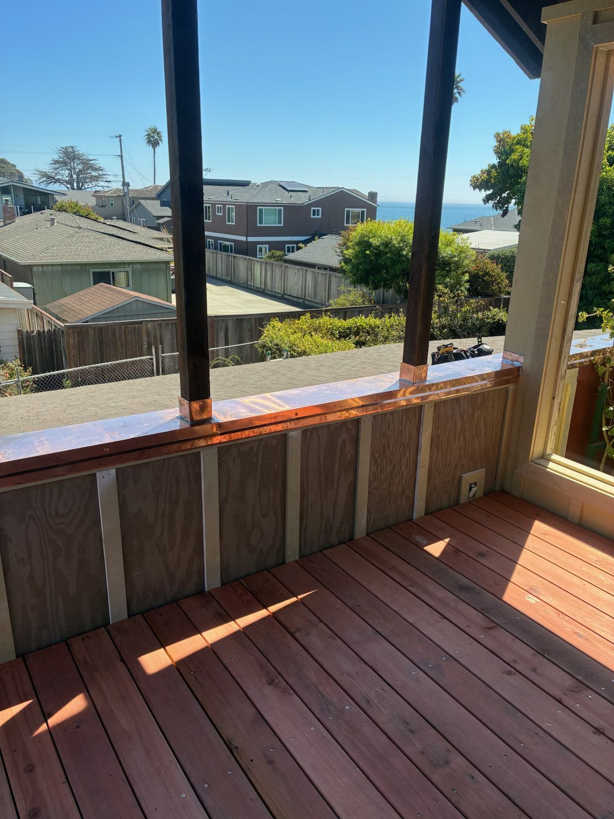 Sunlit screened porch with wood floor, overlooking neighboring houses and a blue sky.