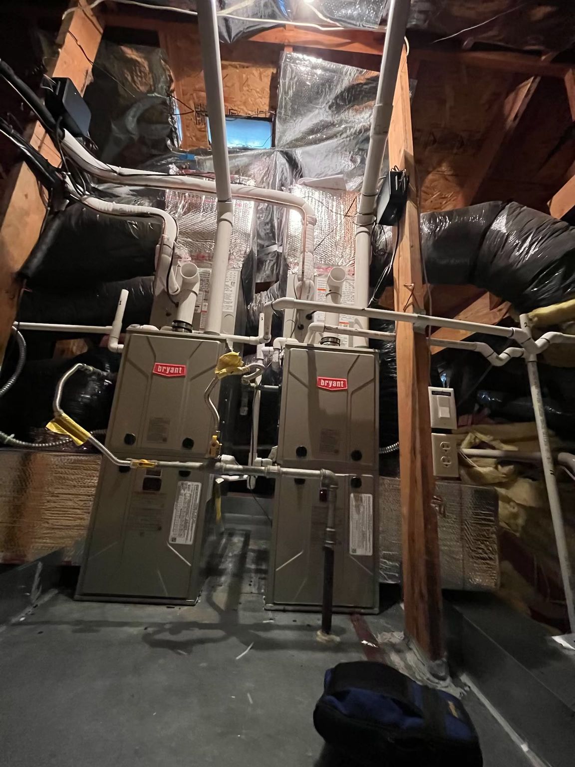 Basement furnace room with two metal HVAC units, ductwork, and exposed insulation.