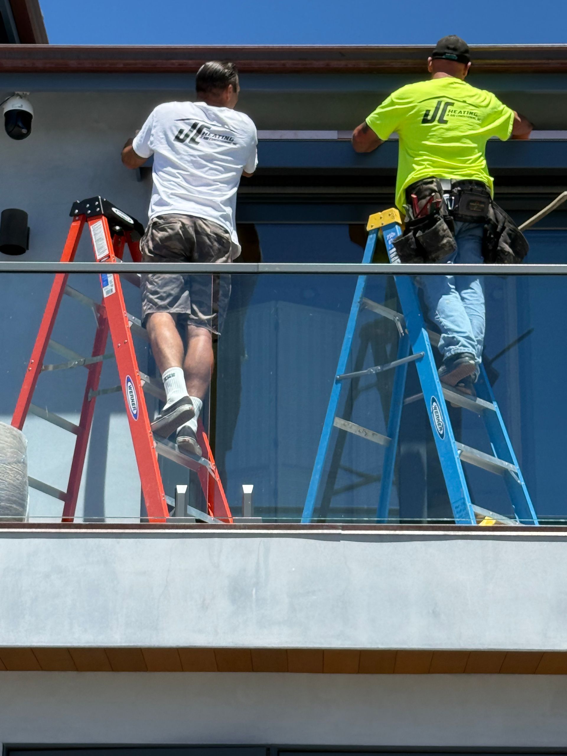 Two workers on ladders painting a building exterior from a balcony