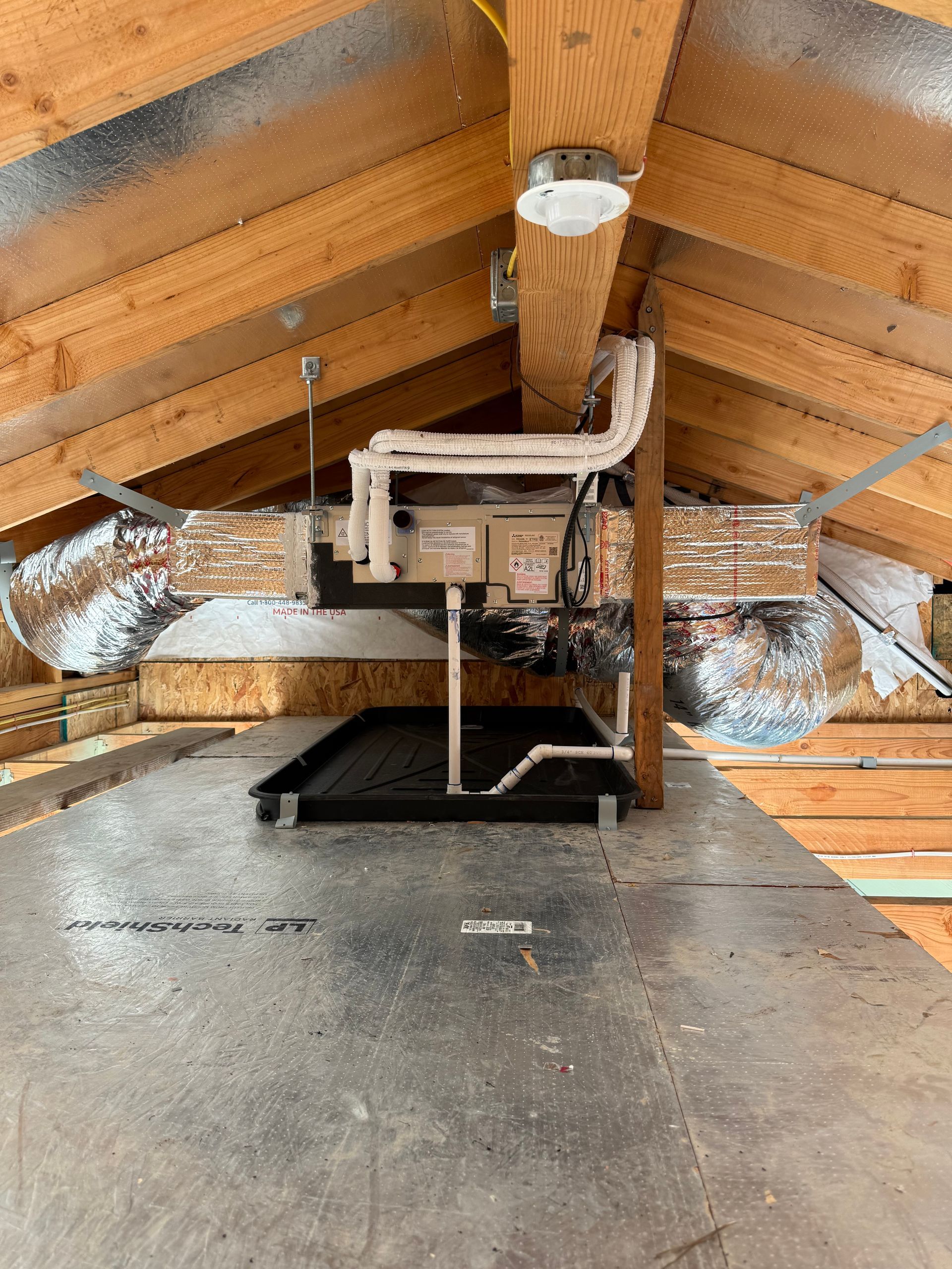 Attic HVAC ductwork and furnace unit beneath wooden roof rafters, with insulation and metal vents