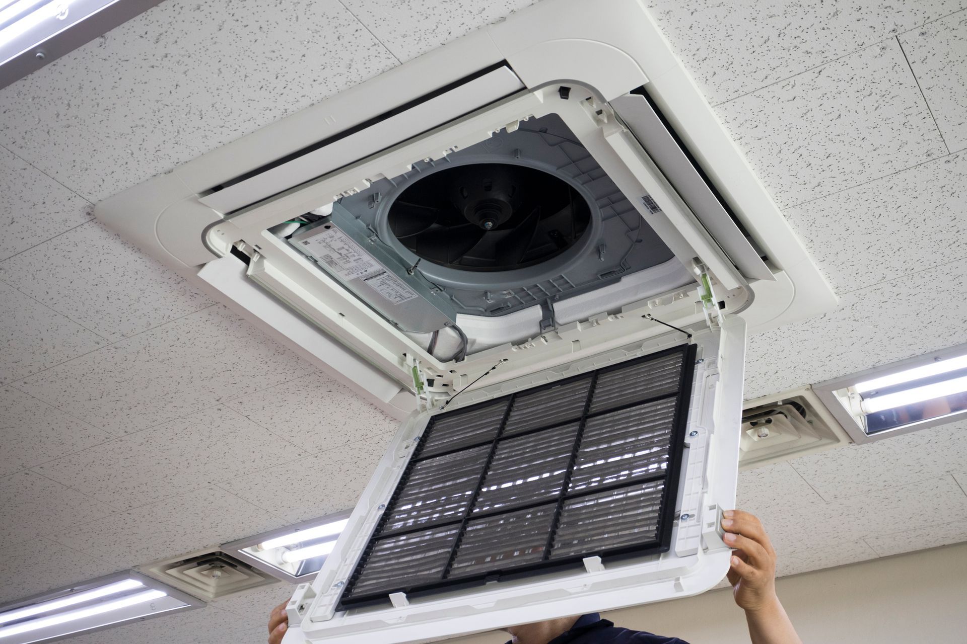 Ceiling-mounted air conditioning unit with open filter being held by a person.