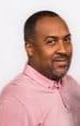 Man wearing a pink shirt smiles at the camera, head and shoulders shot.