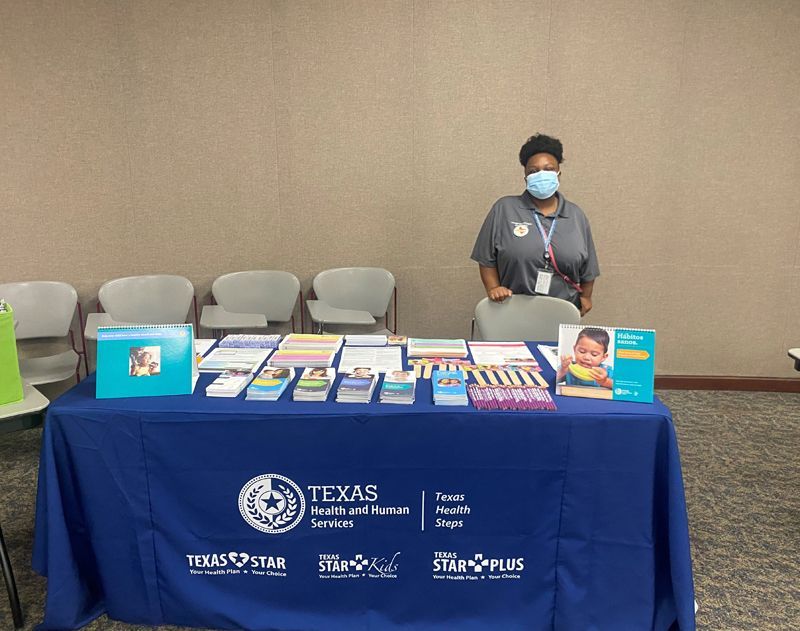 Person at a health services information table with brochures. Table has a blue cover with the Texas Health logo.