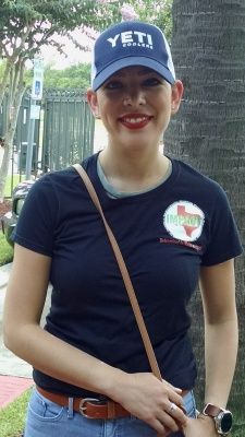 Woman in a blue Yeti hat and t-shirt with a Texas-themed logo; smiling outdoors.
