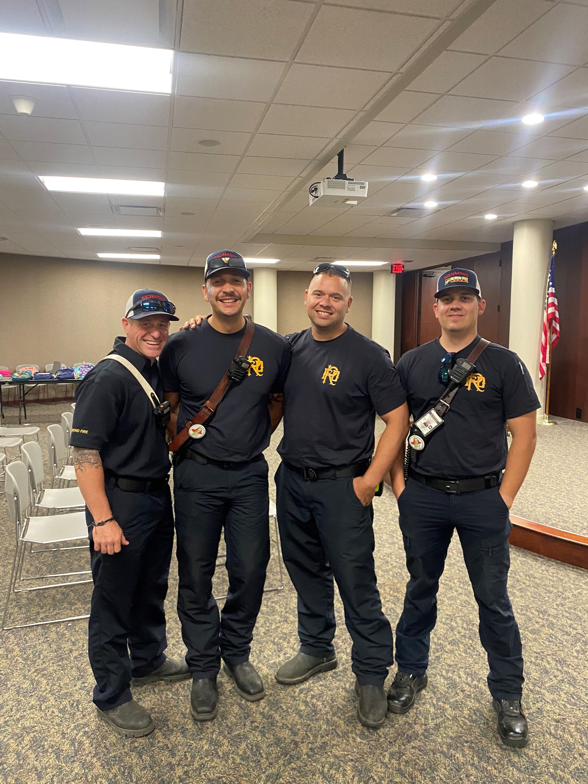 Four men in dark uniforms, standing together indoors.