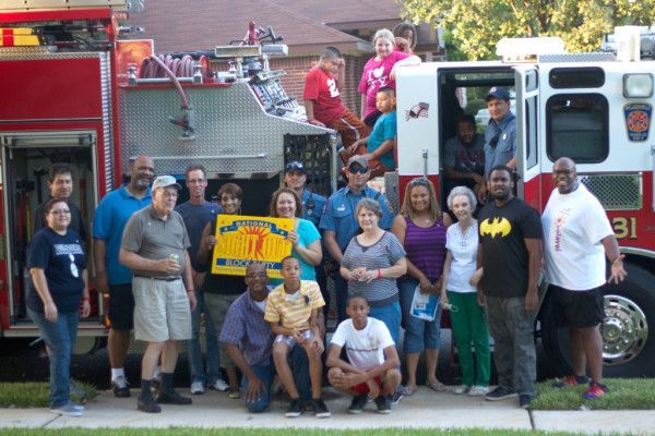 Group of people by a fire truck, some holding a sign, outdoors.
