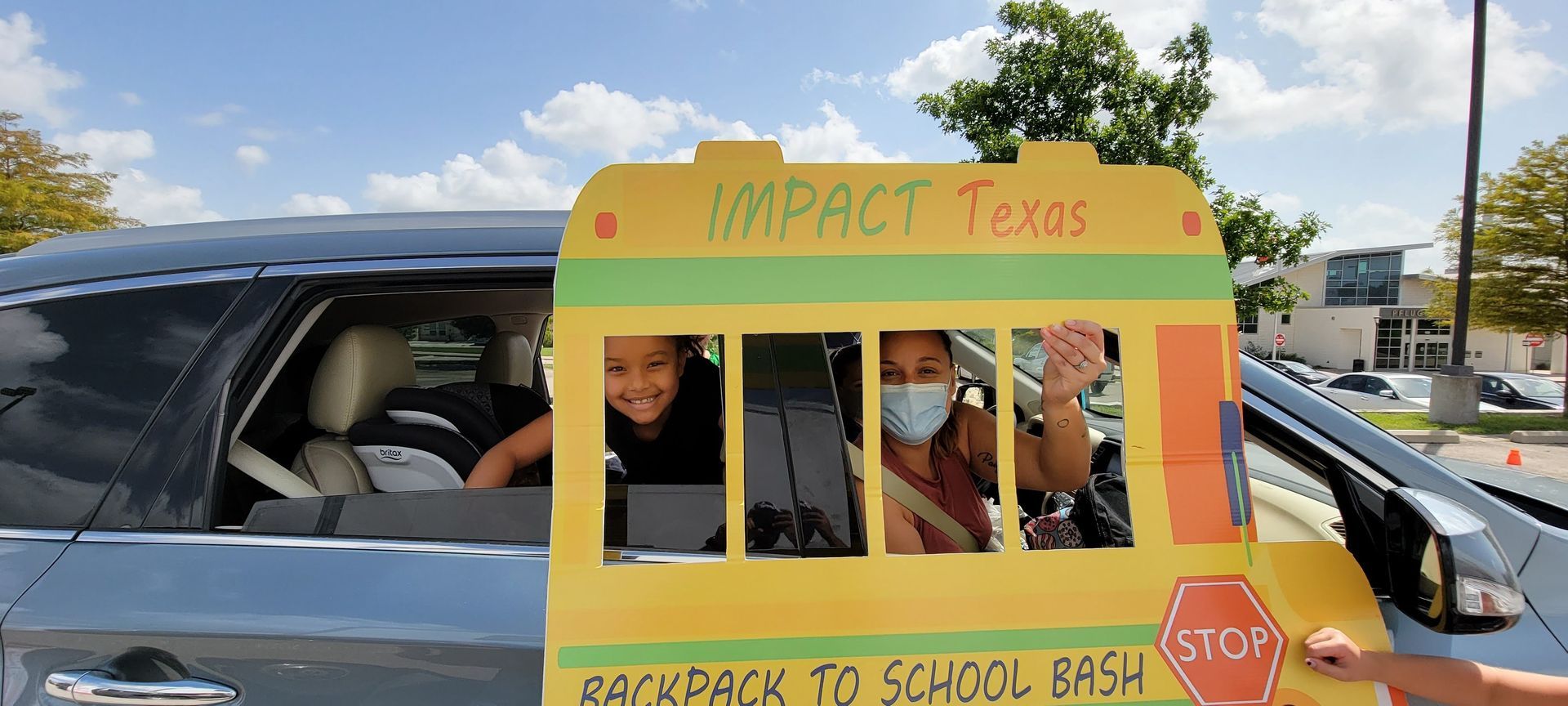 A vehicle decorated as a school bus with two people inside, one wearing a mask, waving.