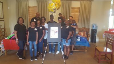 Group of people around a sign on an easel. Balloons behind them. Indoors, neutral colors.