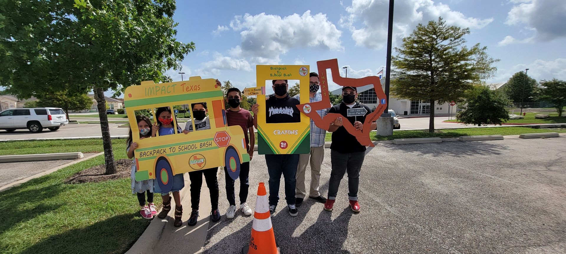 Group of people holding cutouts of a school bus, a sign, and the state of Texas, standing outdoors.