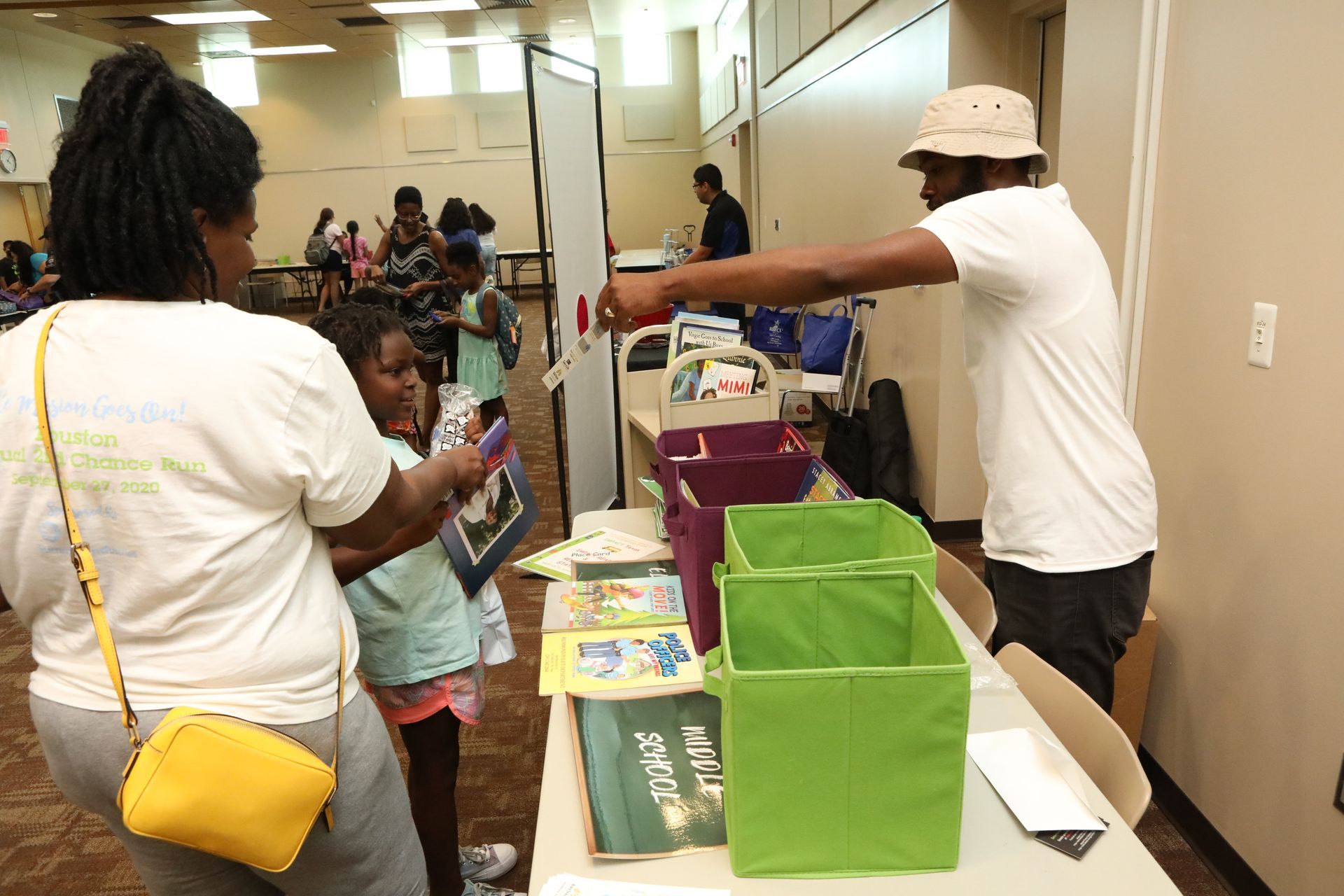 People at a table looking at books. A man points at a book, with green bins on the table.