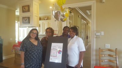 Four people holding a poster, with balloons, in a well-lit home.