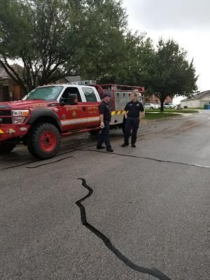 Firefighters standing near a red fire truck on a street, likely after an incident.
