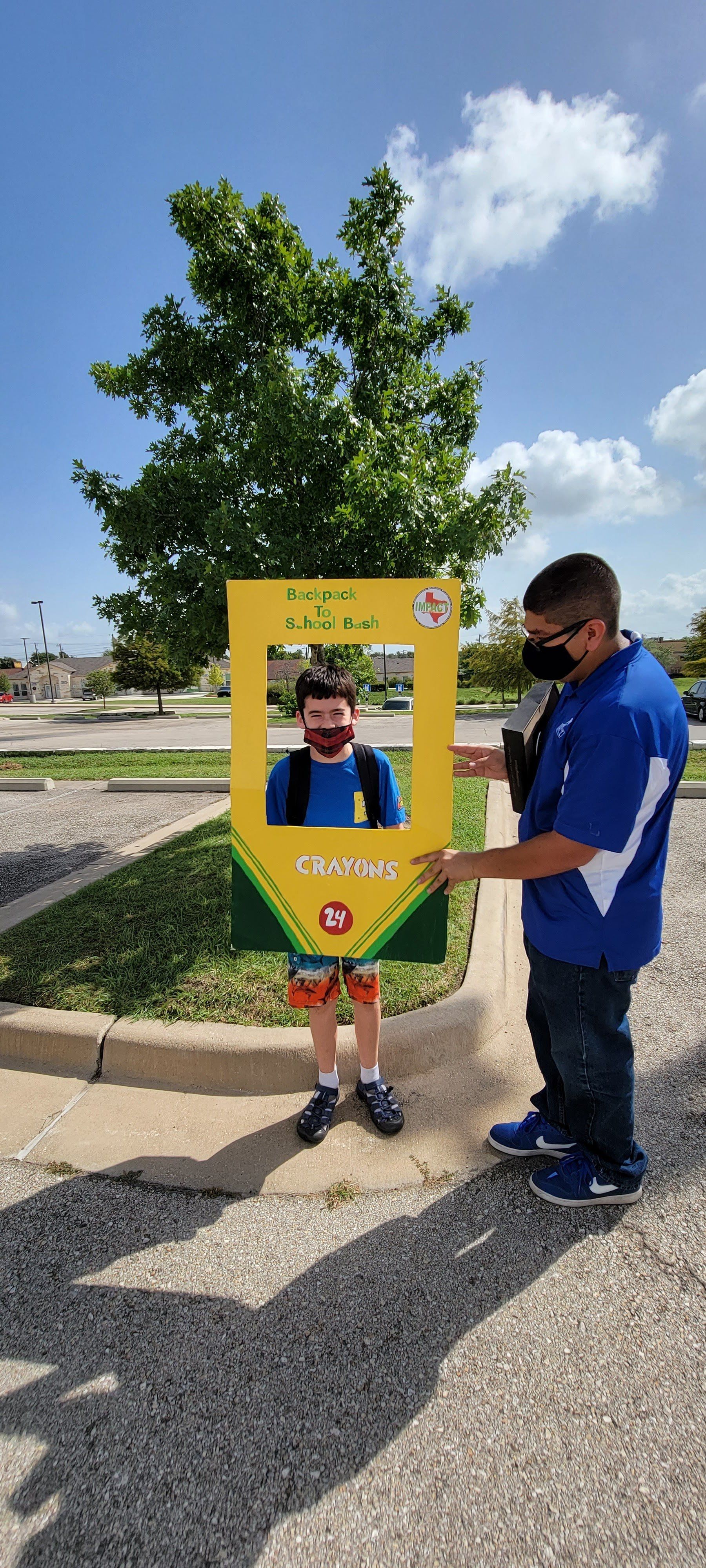 A person framed in a crayon cutout held by another person outdoors on a sunny day.