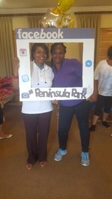 Two people posing behind a Facebook photo frame at Peninsula Park, one in purple, one in white.