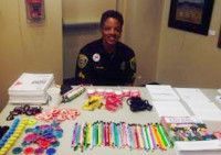 Woman behind a table with colorful bracelets, pens, and papers; smiling, possibly at a community event.