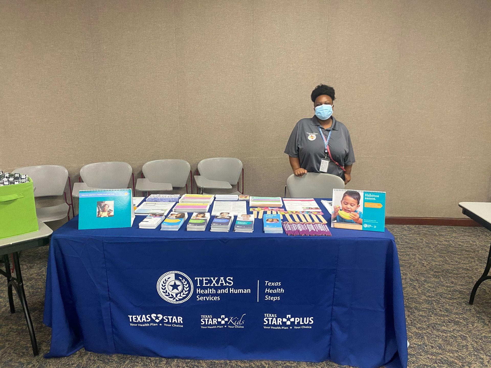 A woman stands behind a table with informational materials, Texas Health and Human Services logo on the front.