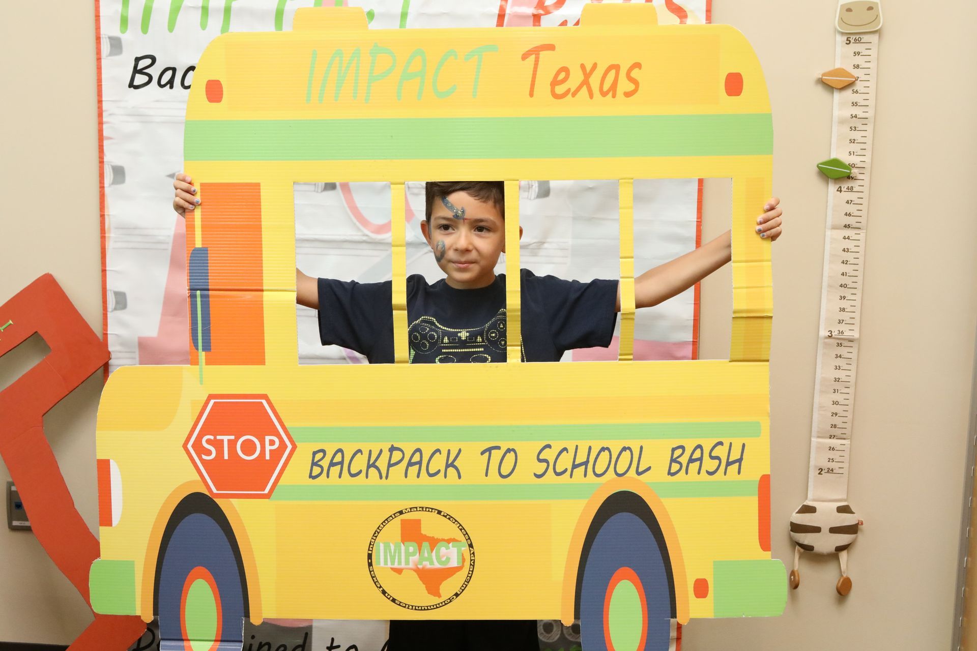 Boy in a yellow school bus cutout, arms raised, at a 