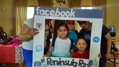Group of kids smiling inside a Facebook-themed photo frame at Peninsula Park.