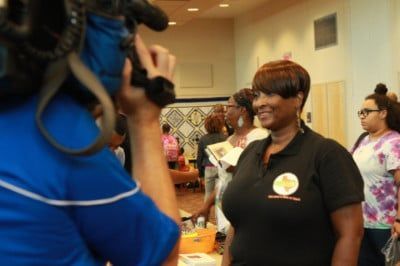 Woman in black shirt with logo being filmed in an event space.