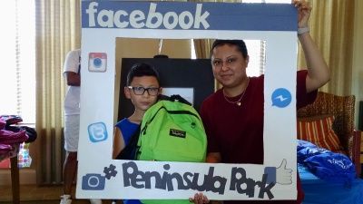 Boy and woman hold a social media frame at Peninsula Park, the boy carrying a green backpack.