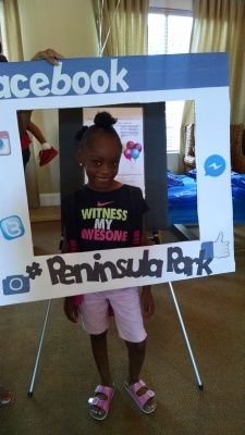 Girl posing inside a Facebook-themed photo frame at Peninsula Park, wearing a black shirt, pink shorts, and sandals.