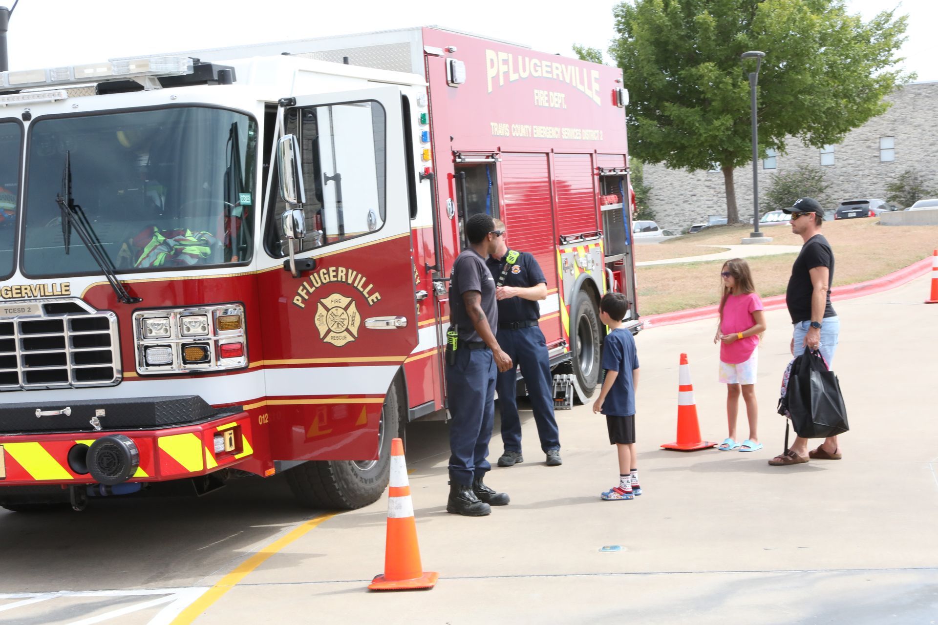 Fire truck and ambulance at an event; firefighters interacting with people near traffic cones.