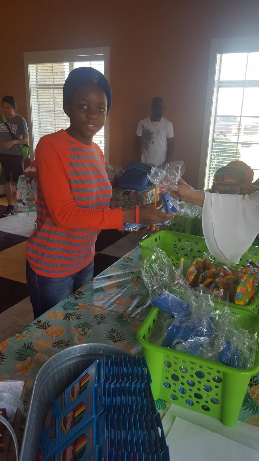 Woman in orange shirt hands items over a table. Others in background.