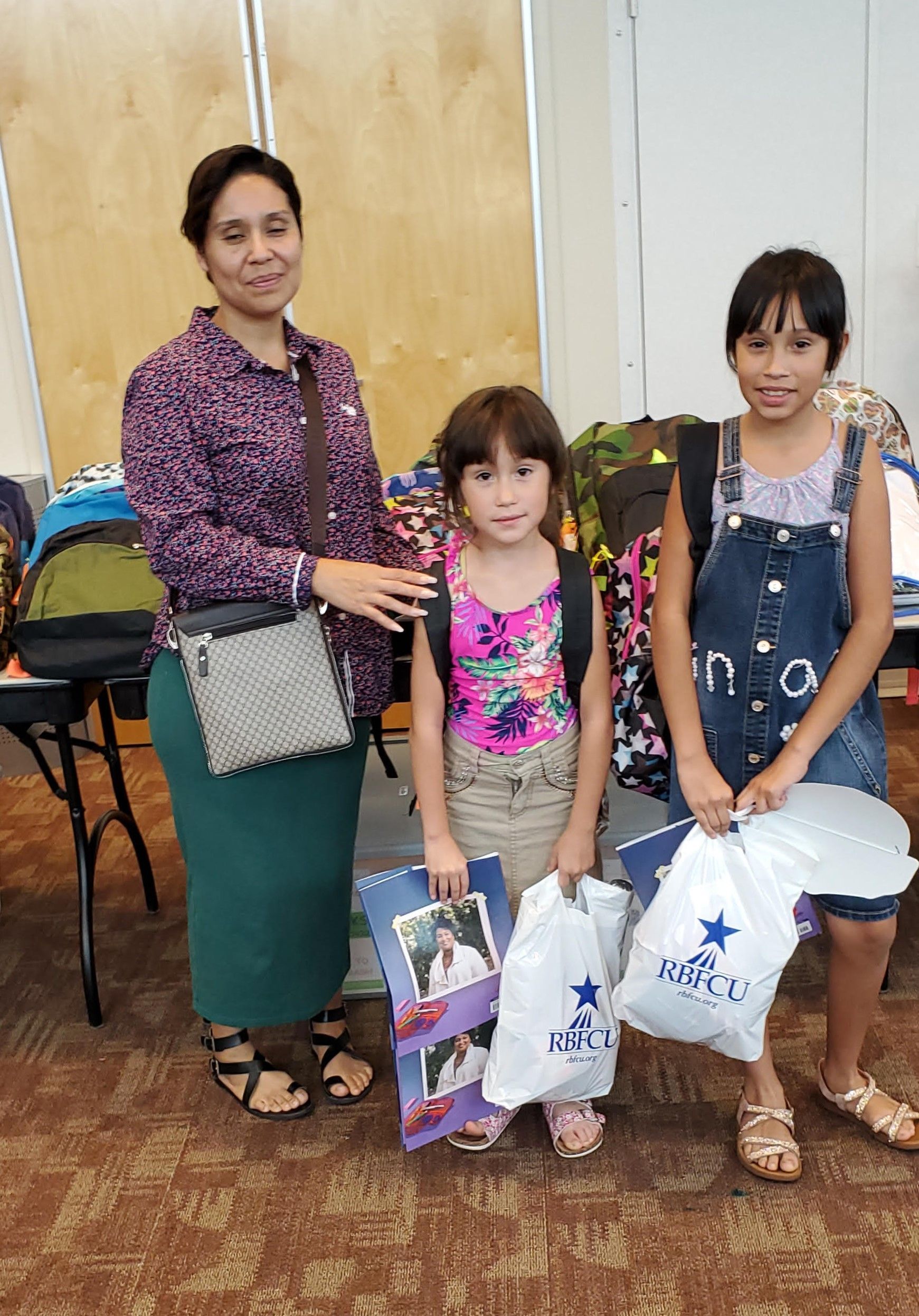 Woman and two children pose with backpacks and school supplies in a room.