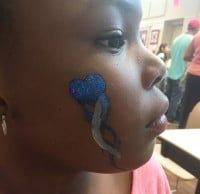 Close-up of a person's face with blue glitter face paint in a ribbon design.