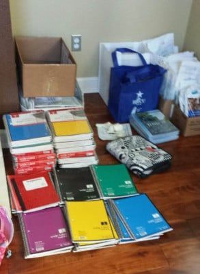 Notebooks, textbooks, and bags on a hardwood floor, preparing for school. Colors include red, blue, green, yellow, and black.