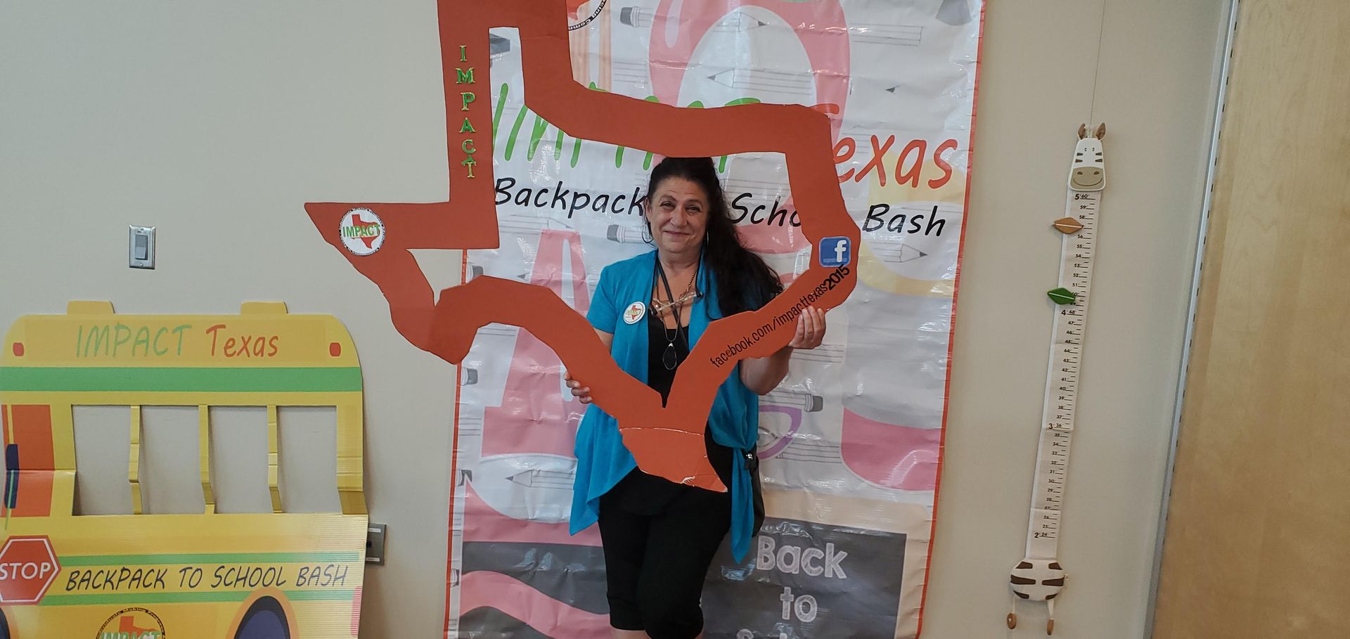 Woman holding a Texas-shaped cutout, in front of a backdrop, and a giraffe wall decoration.