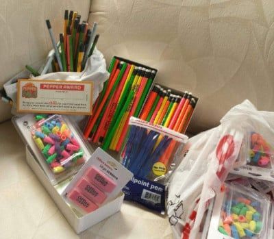 School supplies: pencils, erasers, pens, in a basket and bags, on a couch.