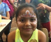 Girl with face painted in white and pink, smiling.