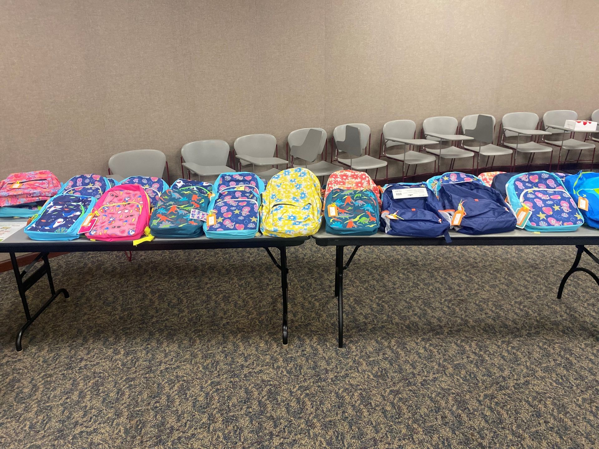 Backpacks on tables in a room with rows of chairs; preparing for school.