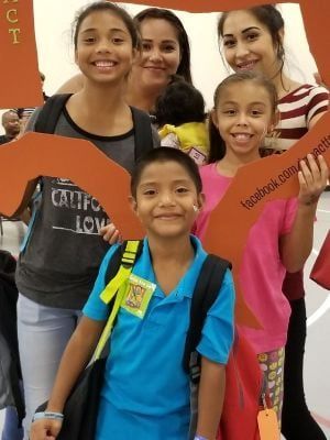 A group of smiling people pose with an orange cutout in a brightly lit room.