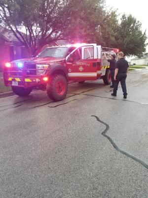 Fire truck with flashing lights parked on a residential street; firefighters near open door.
