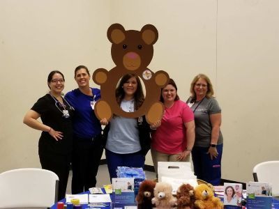 Five healthcare workers pose with a bear cutout and a table of supplies.