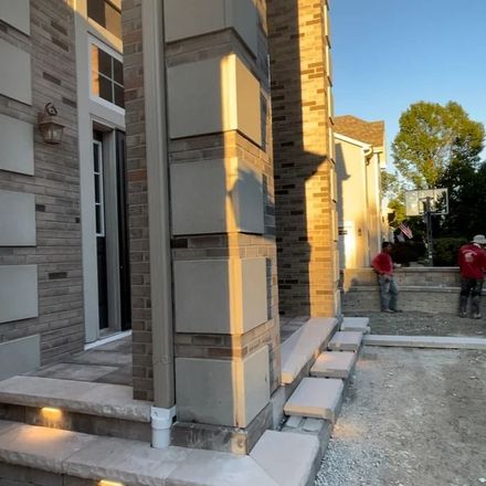 Modern house exterior with a stone column and steps, workers visible in the background
